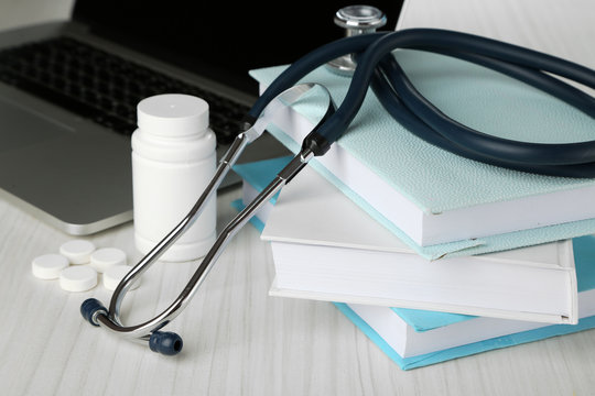 Medical stethoscope with books and laptop on wooden table
