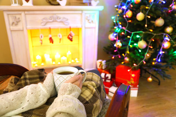 Woman holding cup of hot drink in front of fireplace