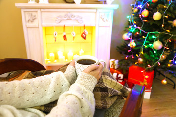 Woman holding cup of hot drink in front of fireplace