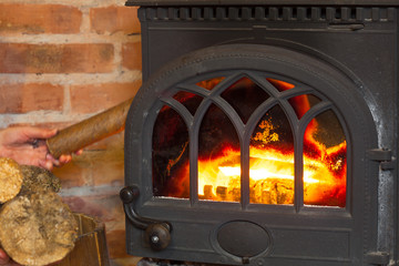Obraz premium Hand putting wood on fire fireplace. Heating.
