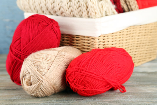 Knitting clothes and yarn in basket, on wooden background
