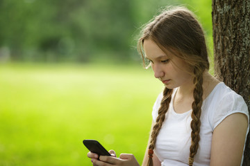 teen girl sitting near tree with mobile phone