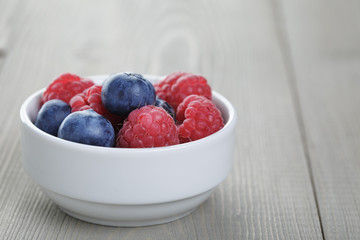 raspberries and blueberries in white bowl