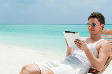 Man sitting with tablet on beach