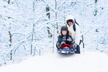 Little boy sledding down a hill with his father helping him