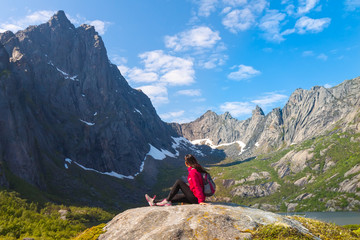 Young tourist woman is sitting  on stone near mountain lake