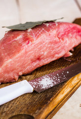 pork on a bay leaf, knife and salt on a wooden board