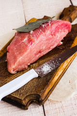 pork on a bay leaf, knife and salt on a wooden board