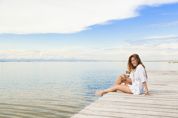 Fototapeta na wymiar Smiling beautiful young woman sitting on a pier and using a mobi