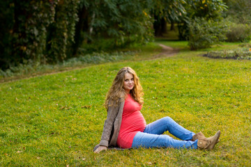 Fototapeta premium Beautiful pregnant blonde lying on green grass