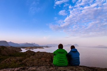 Rear view of two friends sitting together on clief near ocean