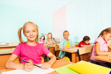 Children write in exercise books and sit at tables