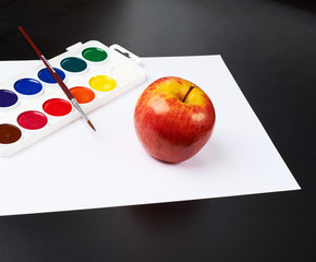 Watercolor set and apple over white paper