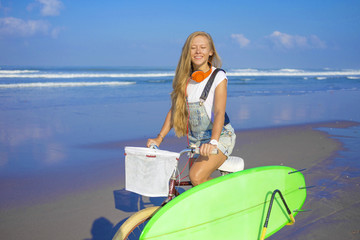 Young girl with surfboard and bicycle on the beach.