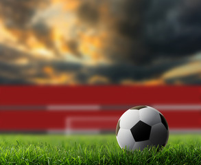 Naklejka premium soccer ball on green grass with sunset background.