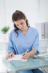 Brunette doctor writing on clipboard