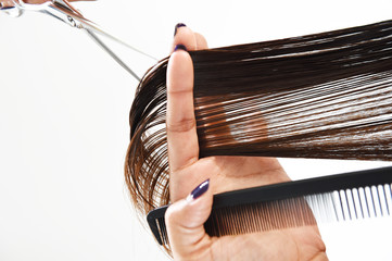 Close up of beautician's hand with a comb cutting hair of woman