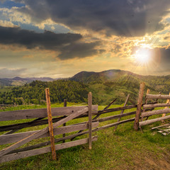 Fototapeta premium fence on hillside meadow in mountain at sunset