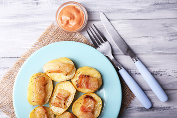 Baked potato with bacon on plate, on wooden background