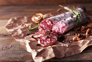 French salami and walnuts on craft paper on wooden background - obrazy, fototapety, plakaty
