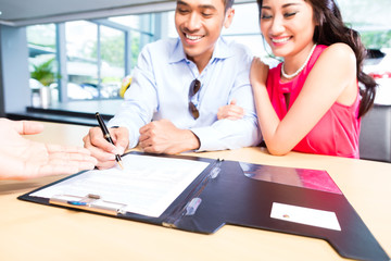 Asian Couple signing sales contract for car at dealership