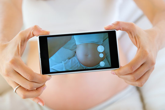 Pregnant woman taking a photo of her belly.