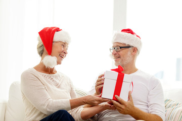 Obraz premium happy senior couple in santa hats with gift box