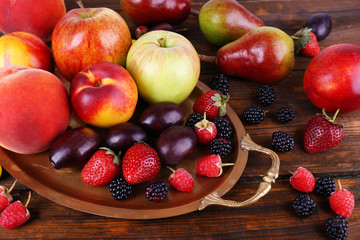 Different berries and fruits on tray on wooden table close-up