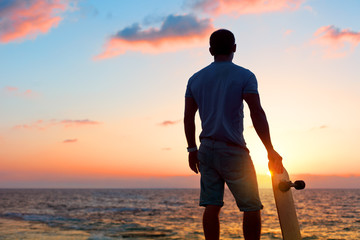 man with skateboard near the ocean in sunset