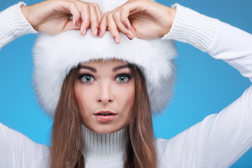 Beautiful girl in a white fur cap and warm clothes on a blue 