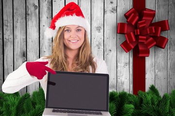 Composite image of festive blonde pointing to laptop