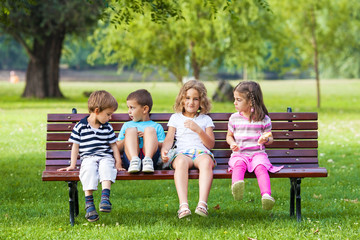 Cheerful Group of Children Sitting on Park Bench