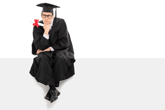 Pensive college graduate sitting on a blank panel