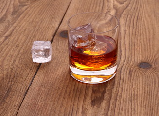 Whiskey with ice cubes in glass on wood background