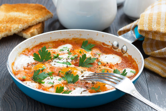 fried quail eggs in tomato sauce with toasts in a frying pan