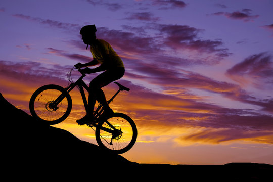 man riding a bike up a hill silhouette in the sunset
