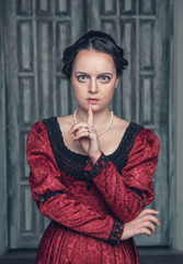 Fototapeta premium Beautiful medieval woman in red dress making silence gesture