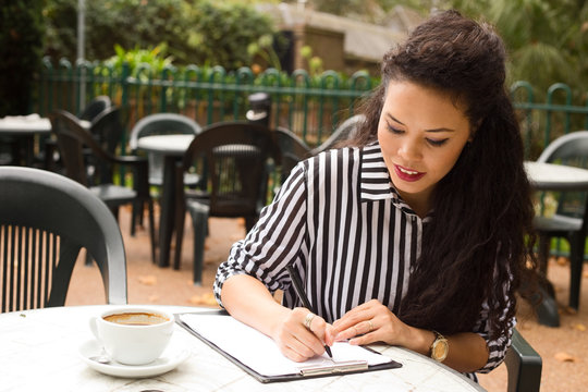 young woman writing on a clipboard with a coffee.