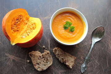 Pumpkin soup in a bowl with fresh pumpkins and brown bread