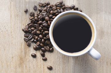 white cup of black coffee with beans on wood table  from above