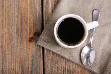 Cup of coffee and coffee beans on napkin on wooden background