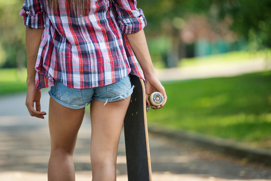 Close up of teenager holding skateboard outdoors in the park.