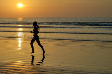 Silhouette of woman jogger running on sunset beach