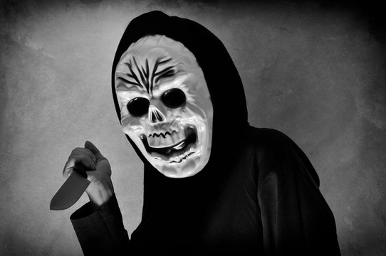 Woman in black with a plastic human skull mask holding a knife