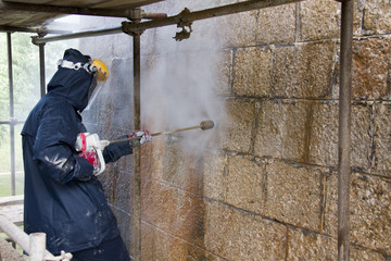 Worker cleans ancient stone wall with high pressure washer from