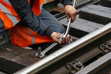 Worker tightens the screw on railroad with two spanners in hands - obrazy, fototapety, plakaty