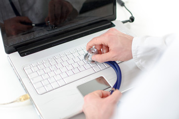 Hand holding a stethoscope on a laptop keyboard