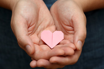 Origami heart in human hands.