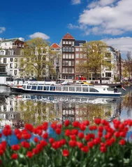 Küchenrückwand glas motiv Amsterdam city with boats on canal against red tulips in Holland © Tomas Marek