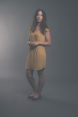 Shy brunette fashion woman wearing yellow dress. Studio shot aga